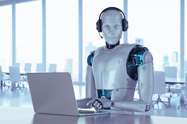 A humanoid robot wearing headphones, sitting at a desk in front of a laptop.