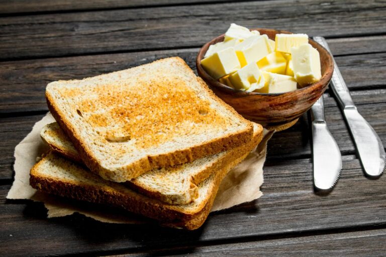 A stack of toasted bread next to a butter knife and a bowl filled with pats of butter.