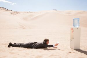 A man in a suit crawling through the desert toward a water cooler.