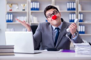 A man with a red clown nose sits behind a work desk.